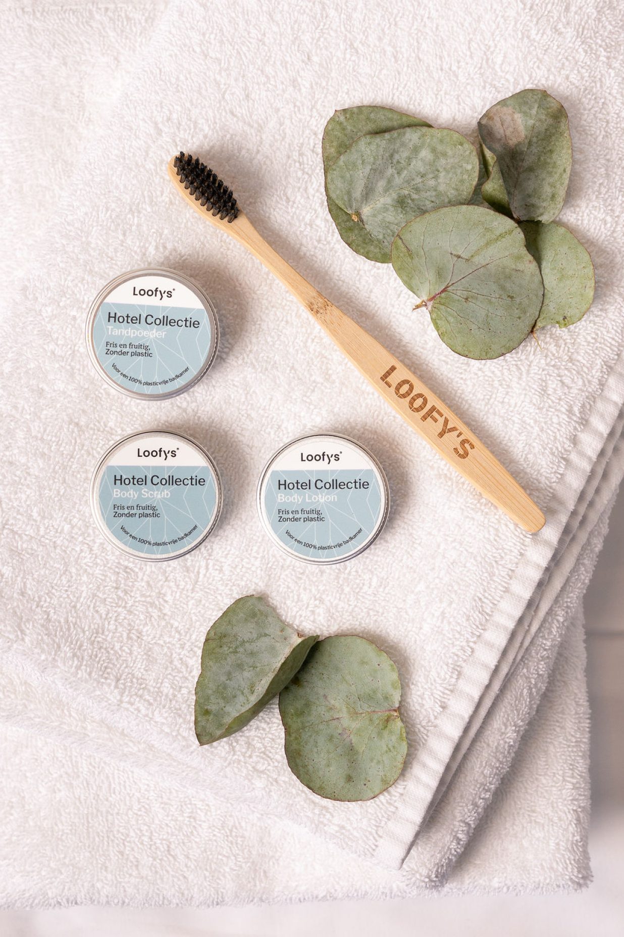 Loofys-giftsets-hotel collectie-tandpoeder, body lotion en body scrub met tandenborstel op stapel handdoeken, met eucalyptus-staand